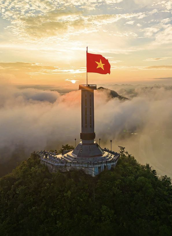 In the soft golden light of an April sunrise, the Vietnamese national flag flutters proudly above a sea of clouds