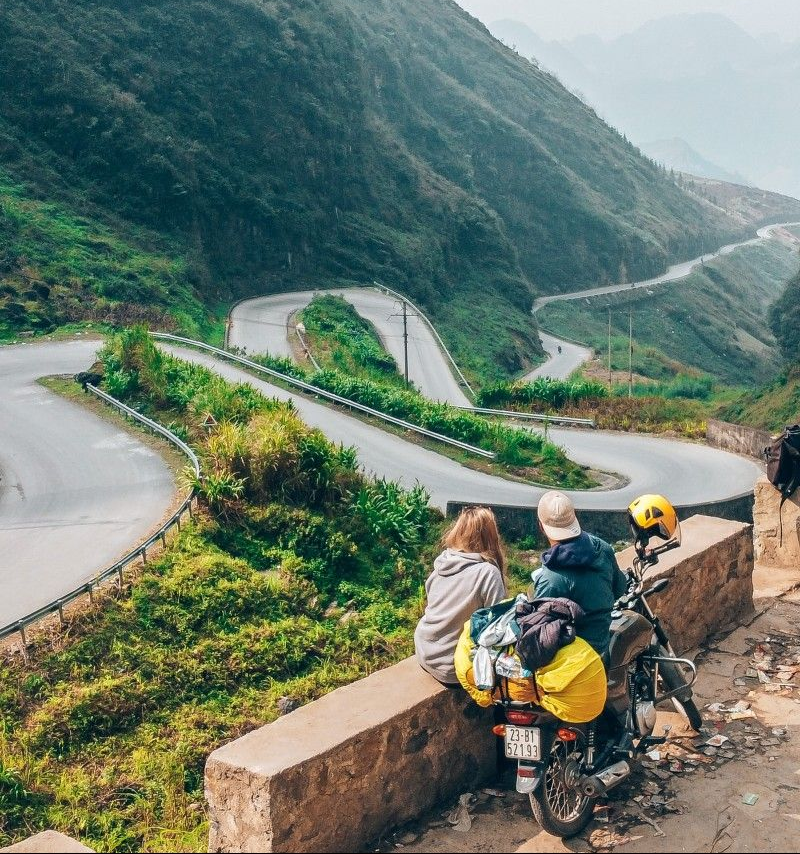 Perched on a rustic stone wall, a couple takes a moment to soak in the breathtaking view of the Tham Ma Pass