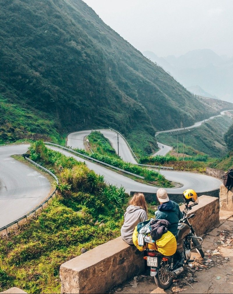 Perched on a rustic stone wall, a couple takes a moment to soak in the breathtaking view of the Tham Ma Pass