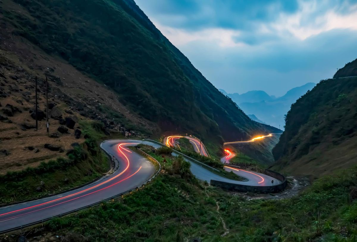Long exposure night photography of the winding Tham Ma Pass with light trails from vehicles on the Ha Giang Loop